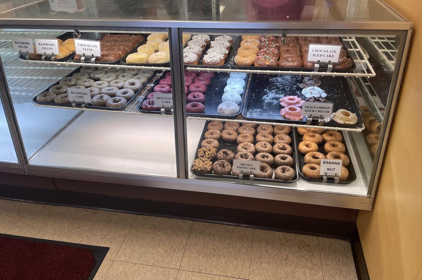 The front glass case with printed labels: blueberry filled, raspberry filled, chocolate fluff, red velvet cake, devils food cake and banana nut.