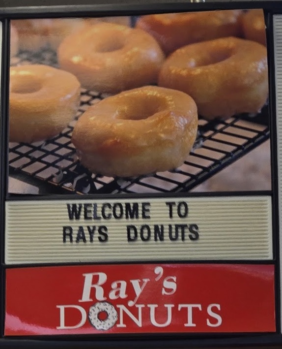 The hanging menu board at Ray's: a donut photo above the words Welcome to Rays Donuts and the red Ray's Donuts sign.
